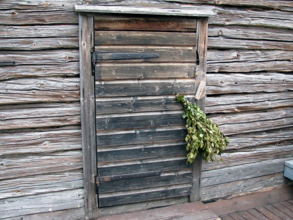 Door leading into a Finnish smoke sauna with a bundle of birch branches on the door handle